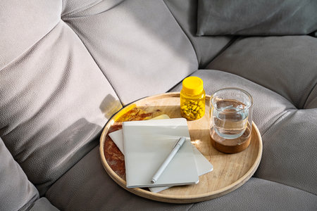 Glass of Water with Medicine and Notebook on Tray Located on Sofa at Home. Relaxing Scene Related to Self Care and Daily Routine.の写真素材