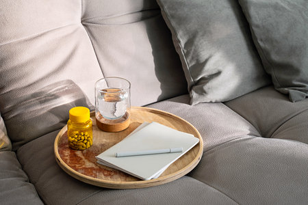 Couch with Tray Holding Medicine Bottle, Glass of Water and Notebook. Daily Routine for Health and Wellness at Home.の写真素材