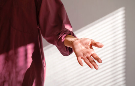 Person Reaching Out Hand in Dappled Shadow of Window Blind on Wall. Offer Help or Assistance. Trust Concept.の写真素材