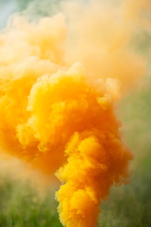 Bright Orange Smoke Rising from Ground Level. Smoke Bomb with Green Grass Background.の写真素材