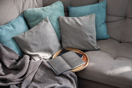 Open Book on Round Tray Rests on a Gray Sofa Draped with Soft Blanket. A Cozy Living Room Scene.の写真素材