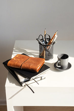 Minimalist Workspace Featuring Desk with Various Notebooks, Coffee Cup and Holder With Pens and Scissors.の写真素材