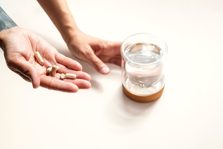 Person Holds Capsules in One Hand and Glass of Water in the Other. Focus on Health and Wellness.の写真素材