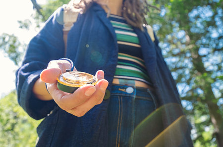 Woman Holds a Compass in Her Hand, Surrounded by Green Trees in a Sunny Outdoor Setting.の写真素材