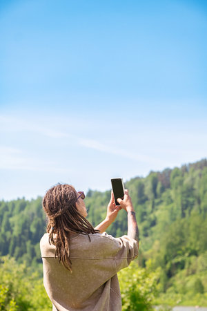Woman Tourist Capturing View of Mountain Landscape with Smartphone. Travel and Photography Concept.の写真素材