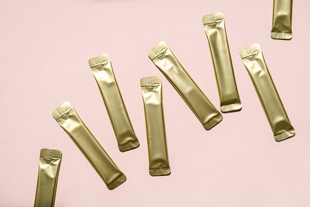 Gold Stick Sachets Scattered on Pink Background. Product Packaging for Instant Coffee or Dietary Supplement.の写真素材