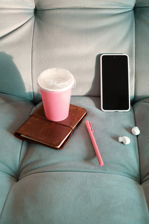 Essentials for Work or Study on a Sofa. Coffee, Smartphone, Notebook, Pen and Earphones for Cozy Productivity.の写真素材