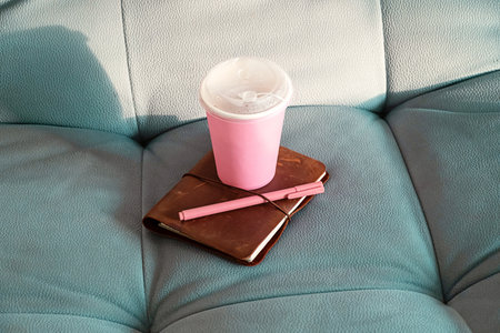 Pink Paper Cup, Brown Leather Journal and Pink Pen Arranged on a Teal Blue Sofa. Cozy Setting for Reading, Writing or Relaxation.の写真素材