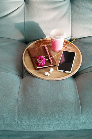 Flat Lay of Wooden Tray with a Notebook, Pen, Coffee, Phone and Headphones on a Teal Couch. Relaxing Home Office Setup for Remote Work.の写真素材
