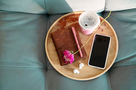 Wooden Tray with Personal Items Including a Phone, Notebook and Drink, Resting on Sofa for Relaxation and Productivity.の写真素材