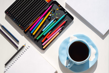 Colorful Pencils, Notebook, Papers and Coffee Cup on White Table with Morning Sunlight. Creative Workspace for Artist.の写真素材
