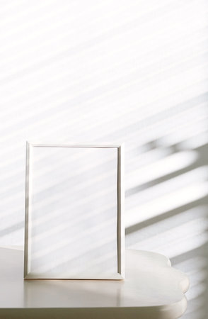Blank White Picture Frame on Minimalist Table with Window Shadow. Home Decor Concept.の写真素材