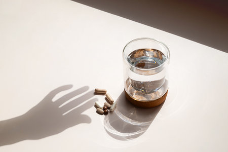 Various Capsules and Glass of Water with Hand Shadow on Light Background. Daily Vitamins and Pills for Medical Treatment.の写真素材