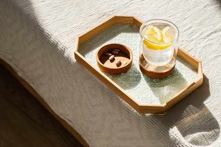Glass of Water with Lemon Slices and Pills on Cozy Bed in Natural Sunlight for Health and Wellness.の写真素材