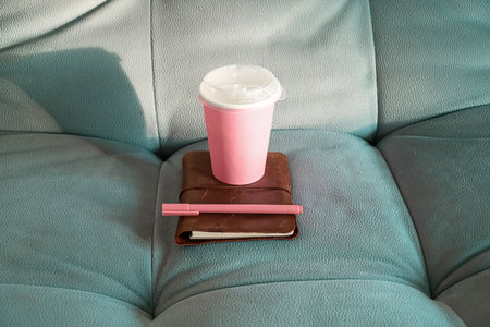 Pink Disposable Cup on Leather Notebook with Pen on a Sofa. Cozy Break for Writing and Drinking Coffee at Home.の写真素材