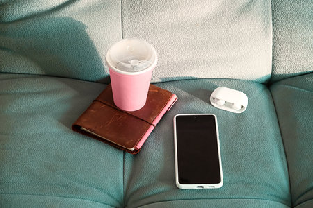 Remote Work. Coffee Cup with Diary, Smartphone and Earbuds on a Comfortable Turquoise Sofa.の写真素材