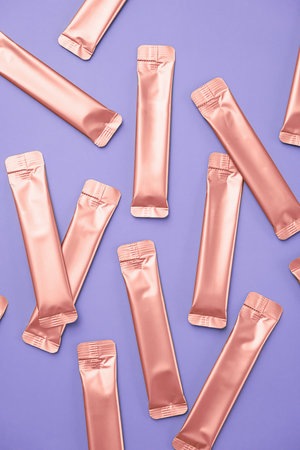 Many Rose Gold Foil Bags for Cosmetic or Food Product on Light Lavender Background. Collagen Stick Pack Mockup.の写真素材