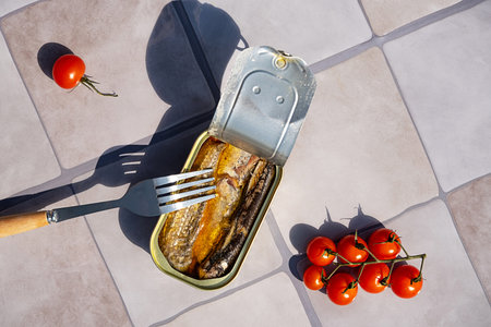 Tin of sardine with fork and tomato on gray tile. Open canned fish for quick dish concept.の写真素材