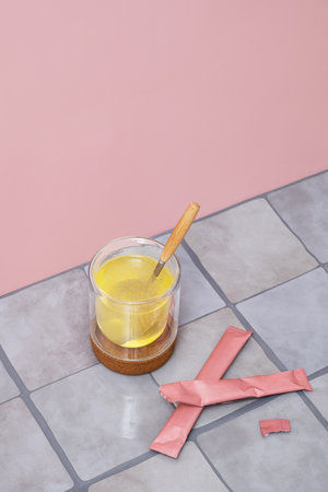 Clear glass with health drink and spoon on a cork coaster next to pink sachets.の写真素材