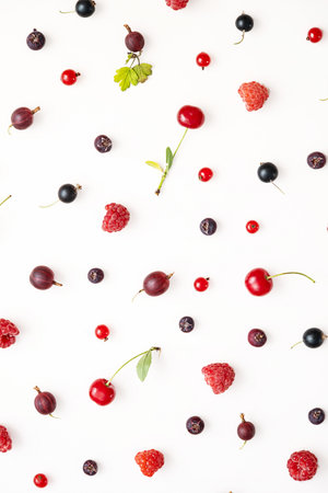 Various fresh ripe berries including cherries, raspberries and gooseberries scattered on a white background.の写真素材