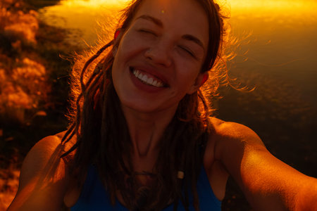 Woman with dreadlocks smiling happily at golden sunset. Beautiful female enjoying good emotion...
