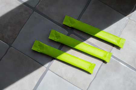 Three green plastic packaging sticks on tile floor with sunlight and shadow. Blank pack mockup for...