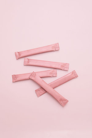 Pink sugar stick pouches scattered on pink background. Sweet snack or beverage additive. Ideal for...