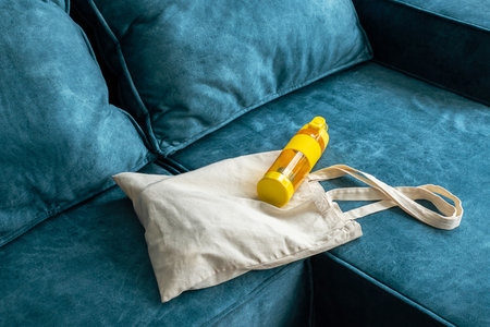 Reusable beige canvas shopping bag and yellow plastic bottle on sofa. Concept of eco friendly sustainable lifestyle.の写真素材