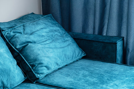 Close up of teal blue couch with fluffy pillows and matching curtains in cozy living room or bedroom.の写真素材