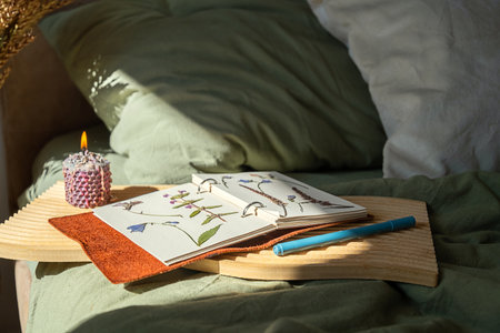 Dried flowers pressed in notebook with burning candle on wooden tray on the bed. Cozy hygge eco living concept.の写真素材