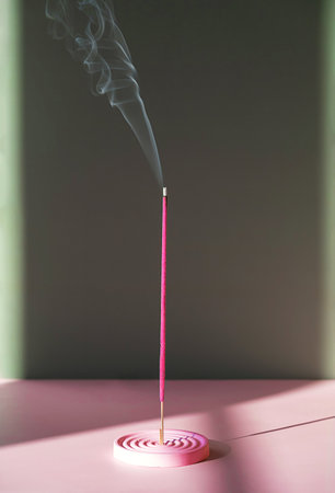 Pink incense stick burning with smoke trail. Aroma for relaxation and meditation. Spiritual practice and home wellness concept.の写真素材