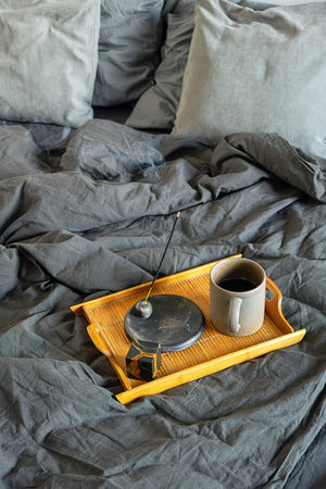 Incense stick burning on bamboo tray with coffee cup on bed. Relaxing morning ritual for mindfulness...