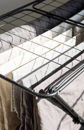 Washed clothes drying on rack near window. Laundry day concept for household chores and sustainable...