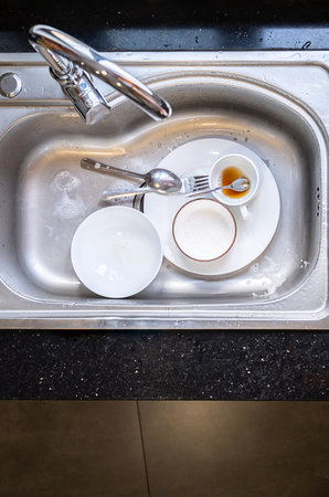 Dirty dishes in kitchen sink. Unwashed plates, bowls and cutlery with leftover food and soap suds. Household chore concept.の写真素材