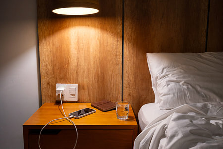 Mobile phone charging on bedside table in comfortable hotel or home bedroom. Modern living and...
