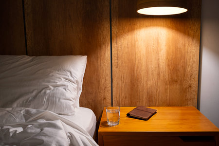 Bedroom scene with nightstand, bed, glass of water and notebook. Home interior for relaxation and...
