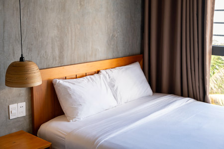 Empty bedroom with clean white lines on wooden bed, cozy hotel room interior, soft pillows and hanging lamp.の写真素材