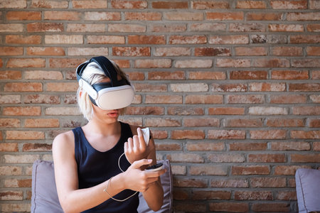Teenager boy with blonde hair wearing virtual reality headset and holding controller. Gaming experience for education and entertainment.の写真素材