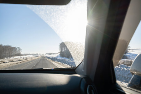 View from inside car of highway with snow covered roadside on sunny winter day, showing travel and journey concept.の写真素材