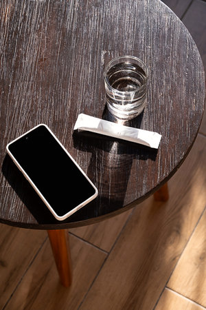Smartphone with blank screen next to glass of water and sachet on wooden table. Mockup for app or product display.の写真素材