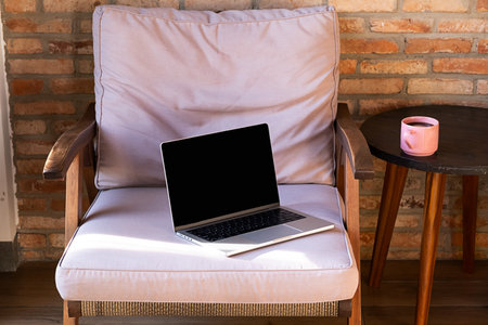 Laptop computer with blank screen mock up on lounge chair next to side table with coffee cup. Remote work and relaxation concept.の写真素材