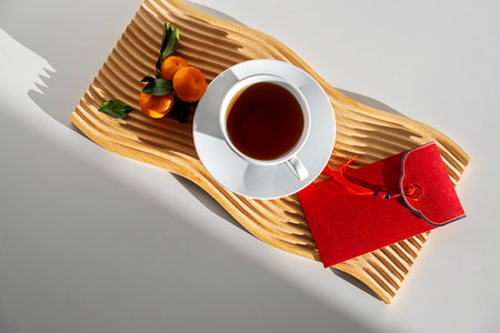 Herbal tea in white cup with tangerine and red envelope on wooden tray. Traditional Chinese New Year offering and celebration concept.の写真素材