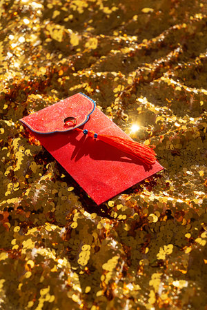 Red envelope with golden tassel lying on sparkling gold sequin fabric for Lunar New Year...