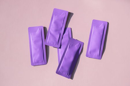 Several purple sachets displayed on light background with copy space. Concept of cosmetic packaging...