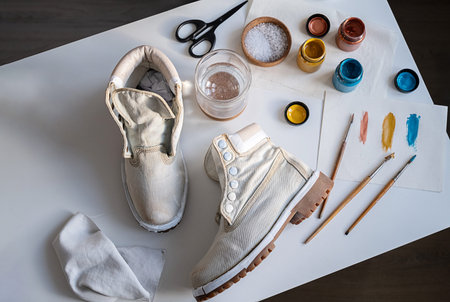 White shoes on white table surrounded by art materials for shoe customization. Workshop concept and...