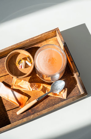 Glass with pink drink, various vitamin pills, and spoon on wooden tray. Healthy lifestyle, wellness,...