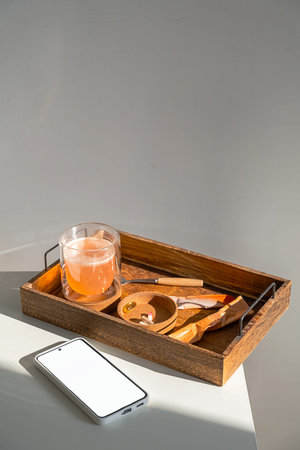 Wooden tray with drink and smartphone on white table. Healthy lifestyle and wellness concept for...