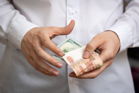 Cash rubles and dollars are counted close-up in the hands of a white man in a white shirt.