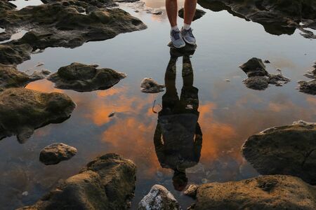 Reflection in the water of a man standing on the seashore. Sunset on a beachの写真素材