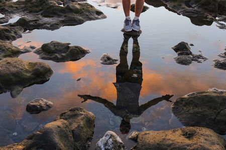 Reflection in the water of a man standing on the seashore. Sunset on a beachの写真素材